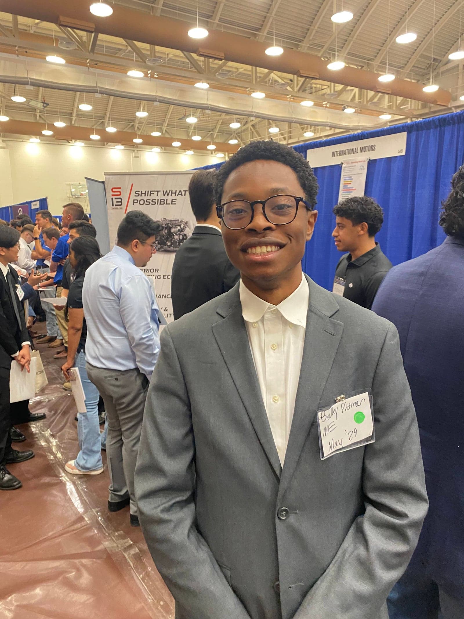 Two NSBE members in professional attire at the Fall 2025 career expo with corporate recruiter booths